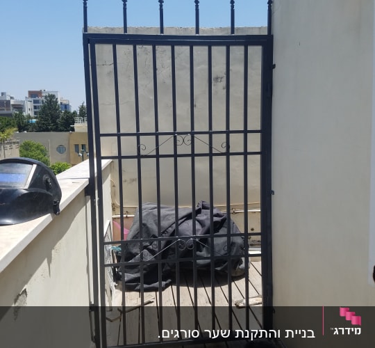 שער מתכת שחור על מרפסת עץ עם פח צבע